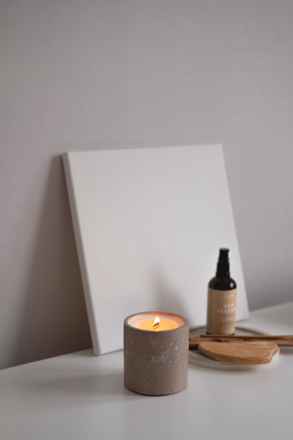 Bougie allumée dans un petit pot gris, près d’une toile blanche