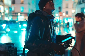 Souleymane avec son vélo de livraison dans une rue de Paris la nuit