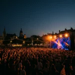 Foule compacte face a une scene de concert en plein air lors de la fete de la musique, eclairage scenique orange et bleu nuit
