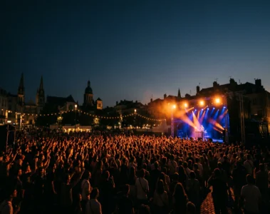 Foule compacte face a une scene de concert en plein air lors de la fete de la musique, eclairage scenique orange et bleu nuit