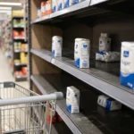 Rayon sucre de supermarche partiellement vide, produits manquants, chariot au premier plan, ambiance magasin
