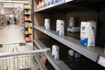 Rayon sucre de supermarche partiellement vide, produits manquants, chariot au premier plan, ambiance magasin