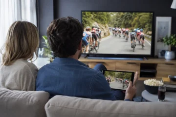 Un couple regarde une course cycliste sur une télévision et une tablette