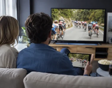Un couple regarde une course cycliste sur une télévision et une tablette