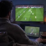 Un spectateur suit du rugby sur un ordinateur portable et une télévision