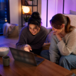 Deux jeunes femmes regardant du streaming sur un ordinateur portable dans un salon