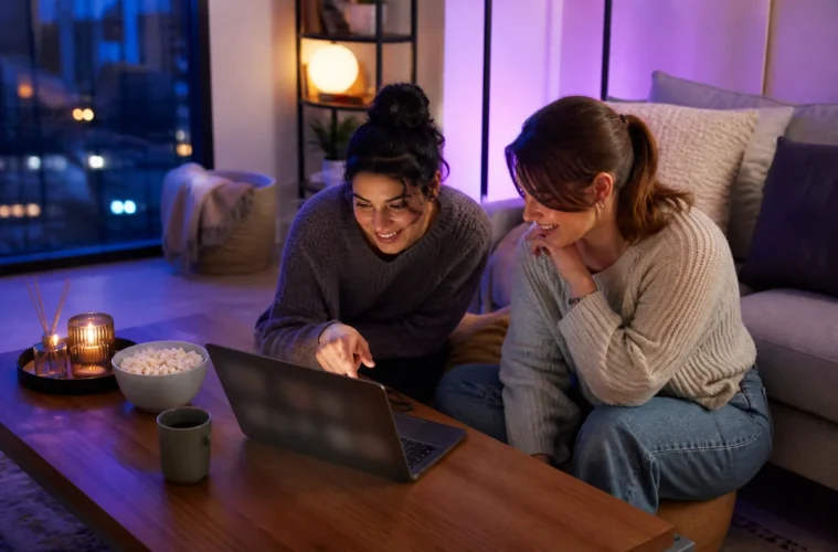 Deux jeunes femmes regardant du streaming sur un ordinateur portable dans un salon