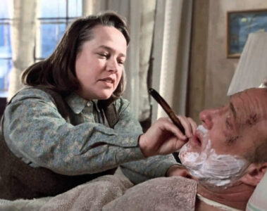 Annie Wilkes, incarnée par Kathy Bates, tient un rasoir près du visage de Paul Sheldon, allongé dans Misery (1990).