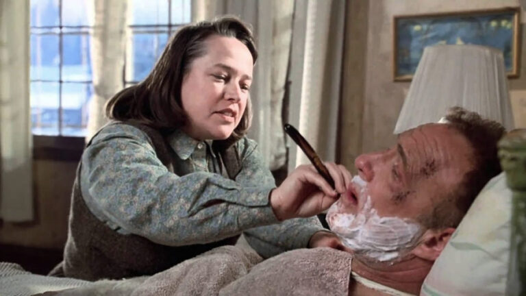 Annie Wilkes, incarnée par Kathy Bates, tient un rasoir près du visage de Paul Sheldon, allongé dans Misery (1990).